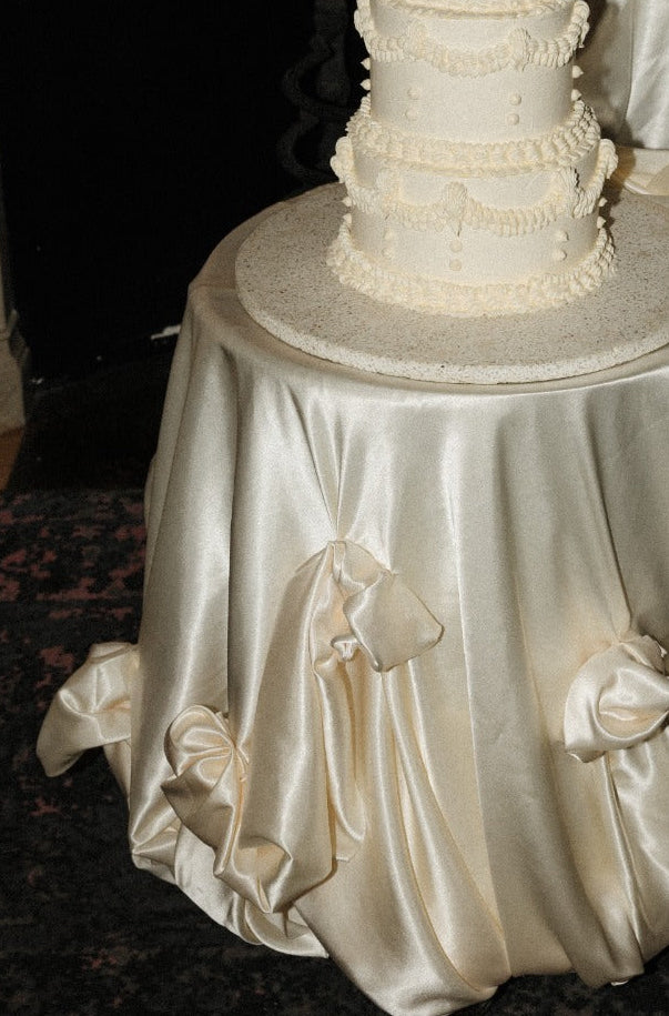 White wedding cake on a table with a decorative chair in front of an ornate fireplace.